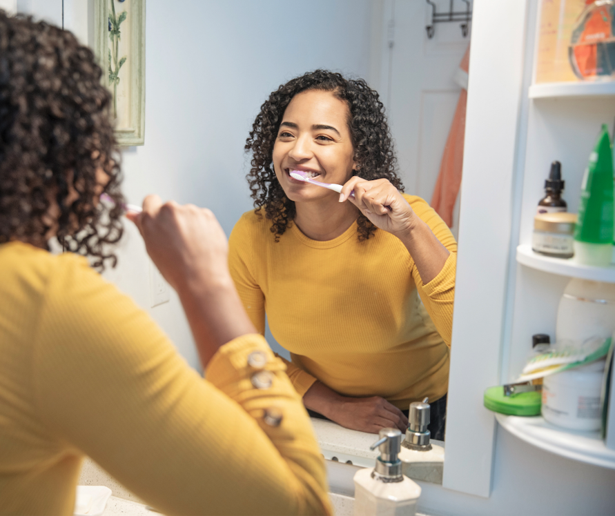 Woman Brushes Her Teeth In Front Of Mirror