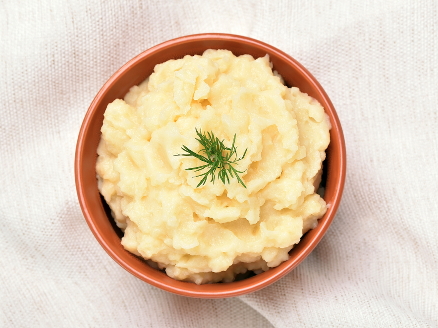 Full Bowl Of Mashed Potatoes Rests on A White Tablecloth 